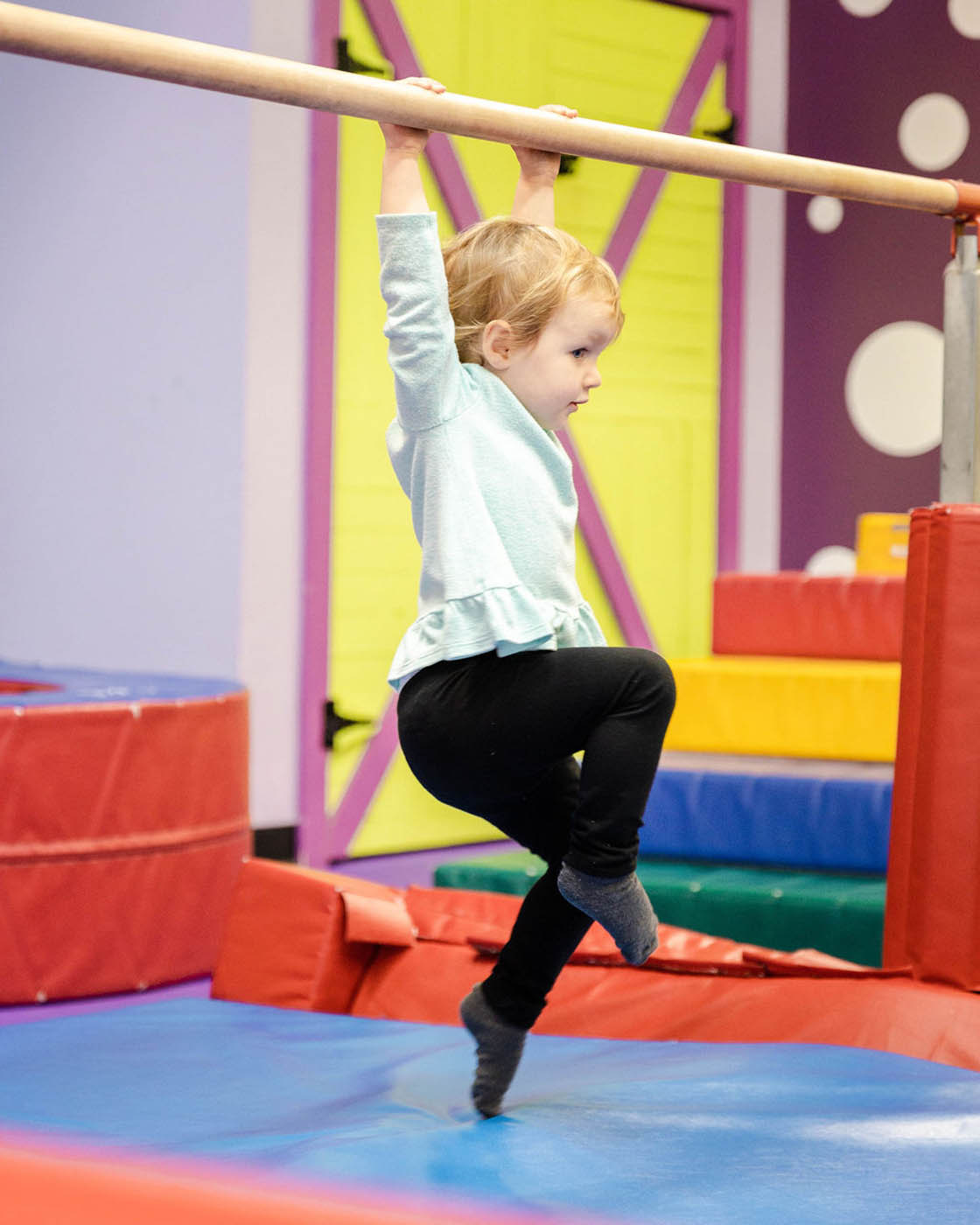 A kid swining from Romp n' Roll gym equipment - safe kids fitness classes in Pittsburgh, PA.