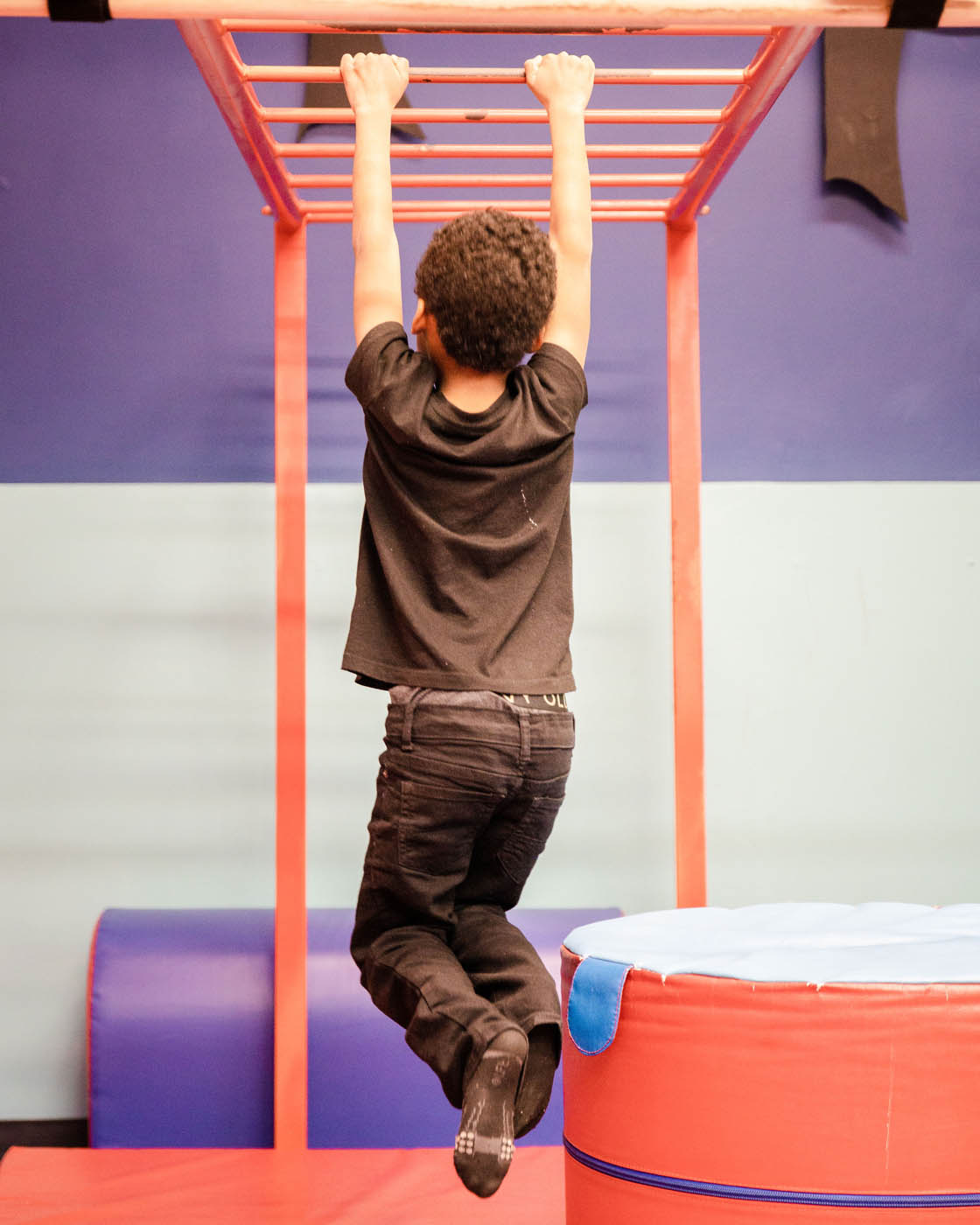 A boy hanging from monkey bars on kid-safe gym equipment at Romp n' Roll in Pittsburgh.