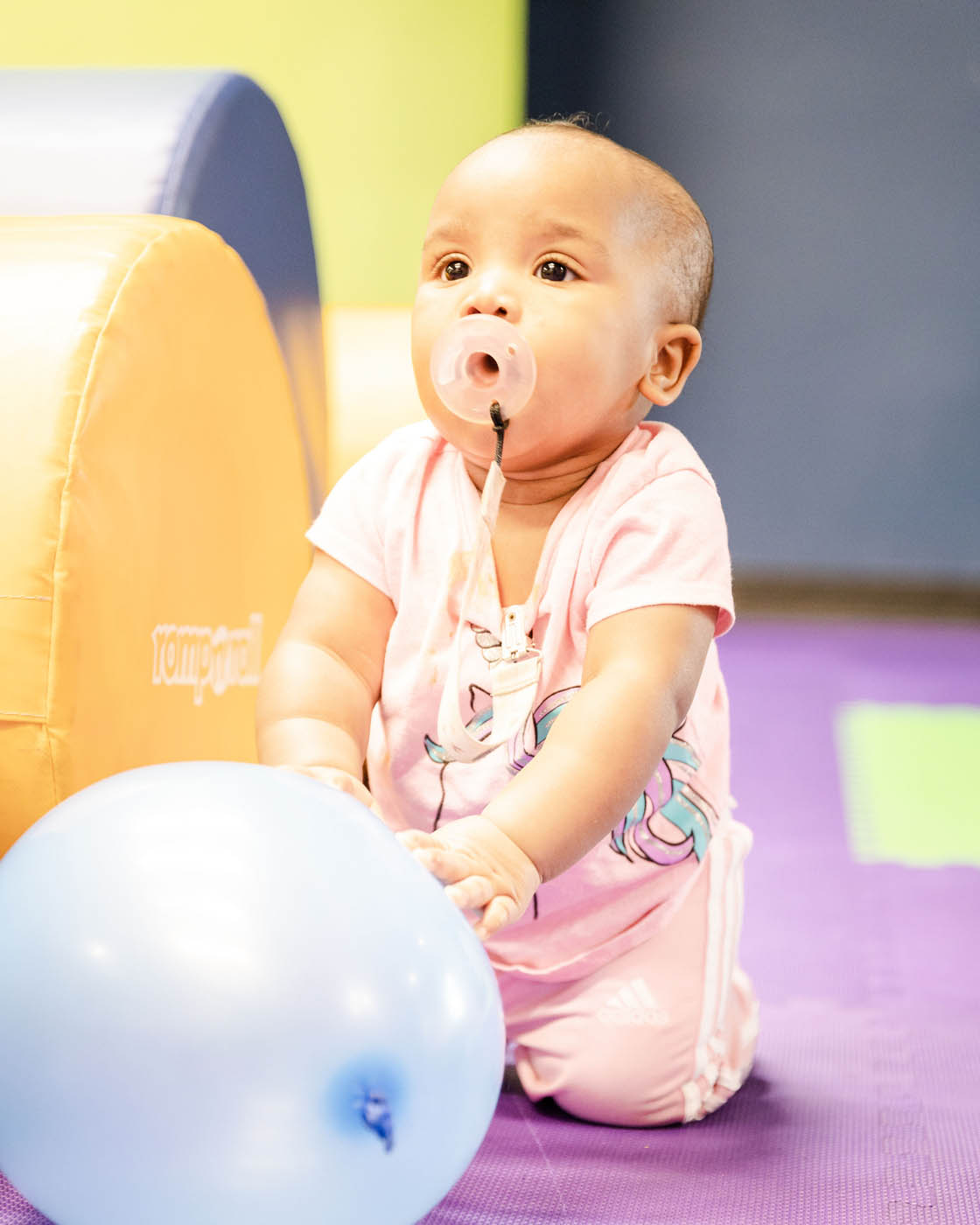 A baby in a gym class working on basic motor skills and enjoying playing with a blue ball - Romp n' Roll in Willow Grove.