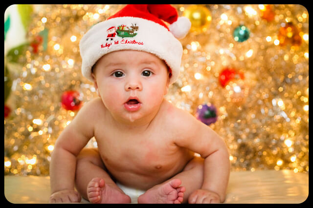 A cute baby in front of a Christmas tree - contact Romp n' Roll in Glen Allen, VA for easy holiday preschool activities!