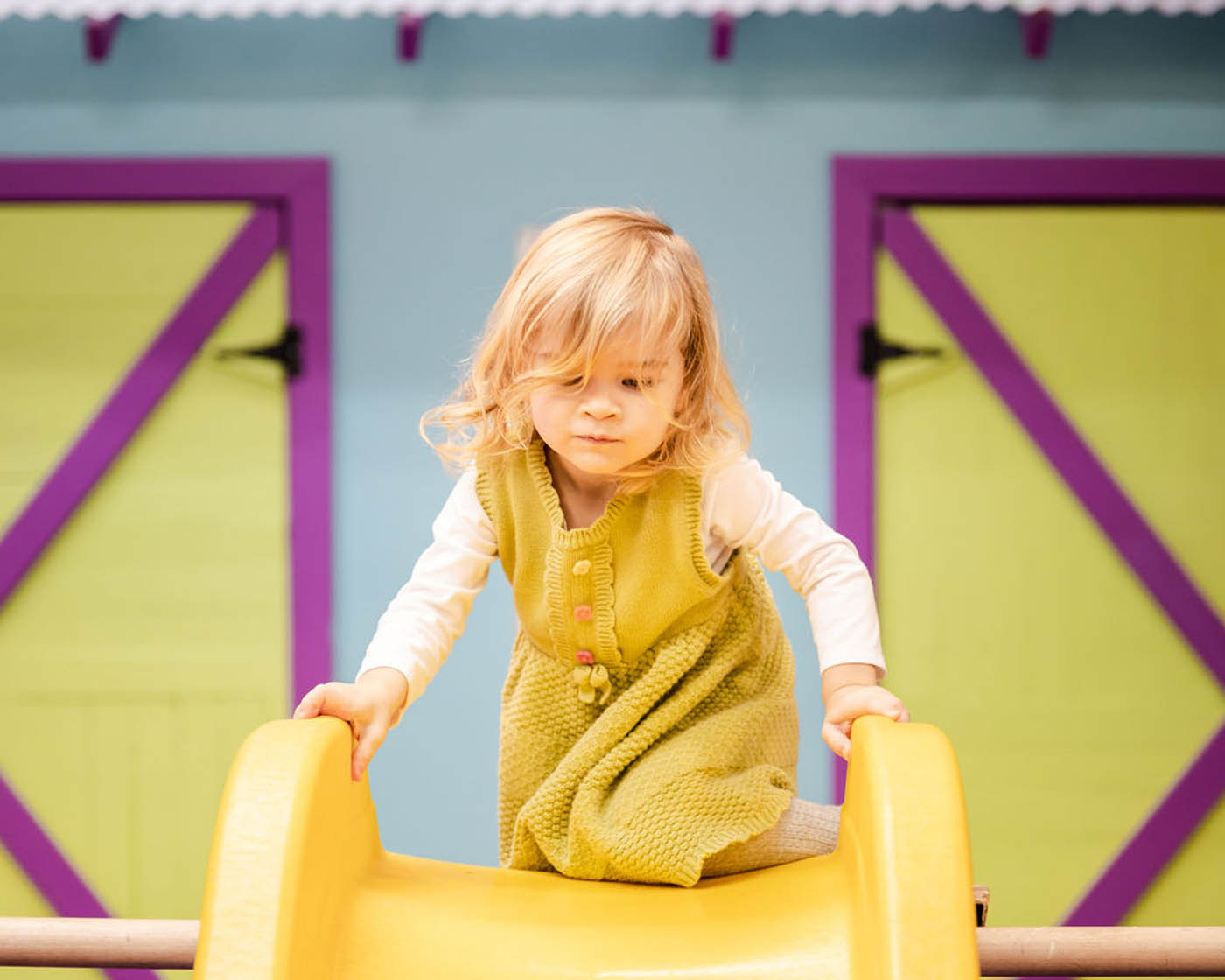 A toddler playing on a yellow slide at Romp n' Roll Northwest Charlotte's classes for 3 year olds in Charlotte, NC